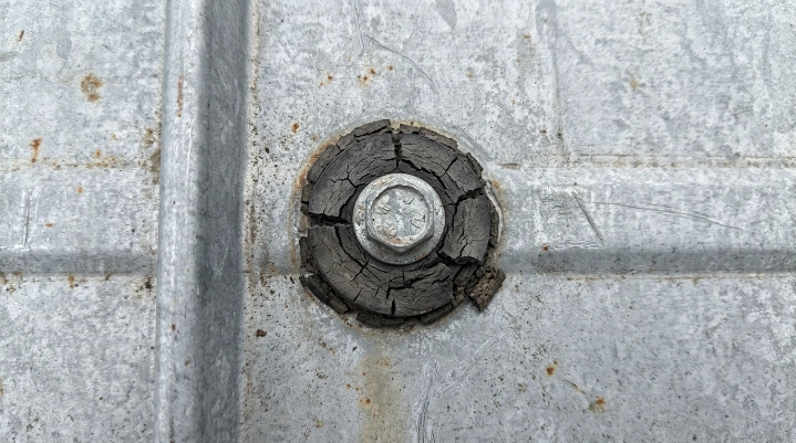 Close-up of a cracked roofing fastener washer on a metal roof that can cause a leak.